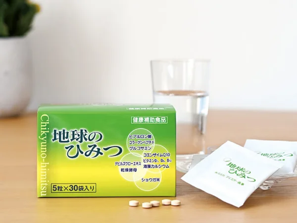 アイスター商事：地球のひみつ（サプリメント）の商品画像、緑色の小箱に「地球のひみつ」と表記、ヒアルロン酸、サーモンコラーゲンペプチド、コエンザイムQ10、S-アデノシルメチオニン、デビルズクローショウガ末などの成分・原材料を表記。小分けの袋とタブレット、背景にはガラスのコップ。